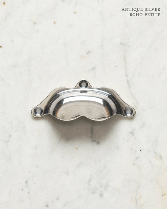 A small bohemian-style cup handle for a kitchen cupboard or drawer with a tarnished silver finish.