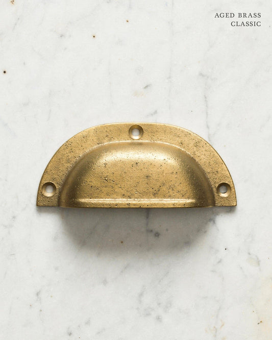Two classic cup handles for a kitchen cupboard or drawer with an aged brass finish. There is a large and a small size.