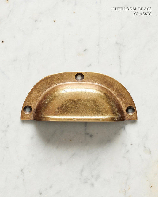 A classic cup handle for a kitchen cupboard or drawer with a warm burnished brass finish.