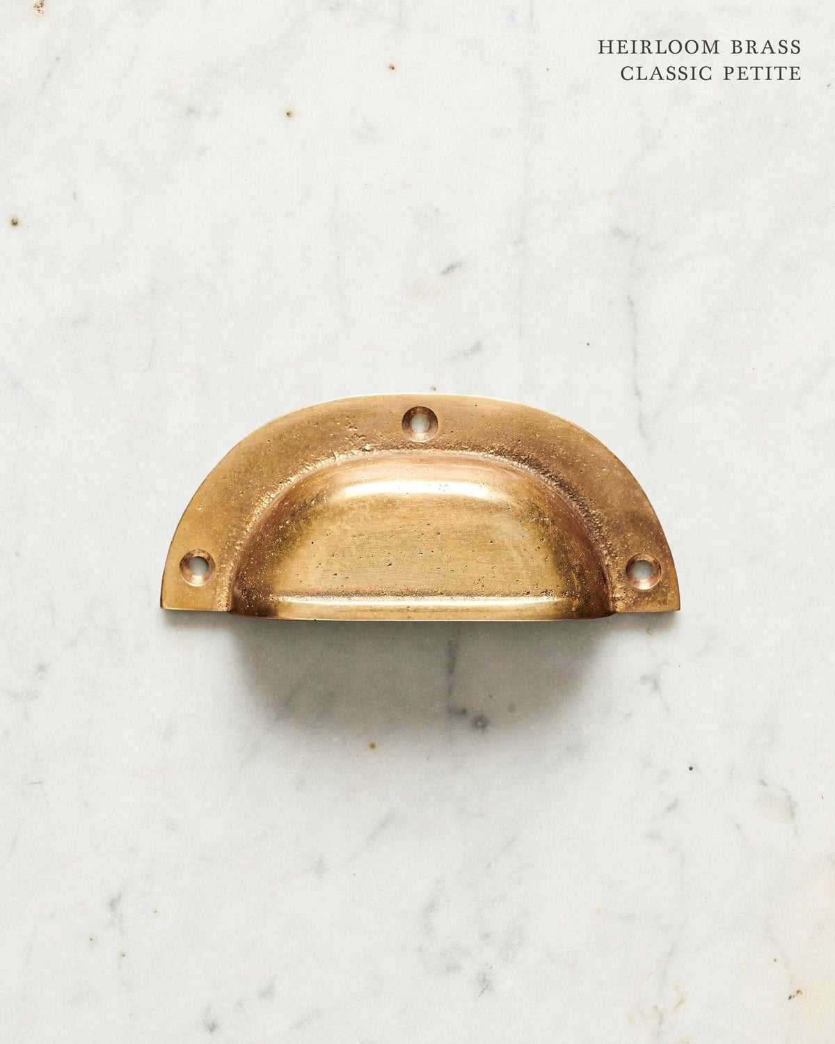 A small classic cup handle for a kitchen cupboard or drawer with a warm burnished brass finish. TEST
