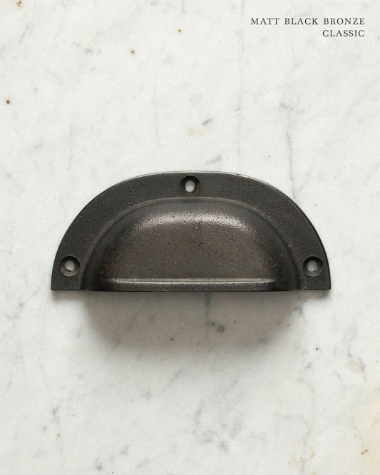 Two classic cup handles for a kitchen cupboard or drawer with a matt black bronze finish. There is a large and a small size.