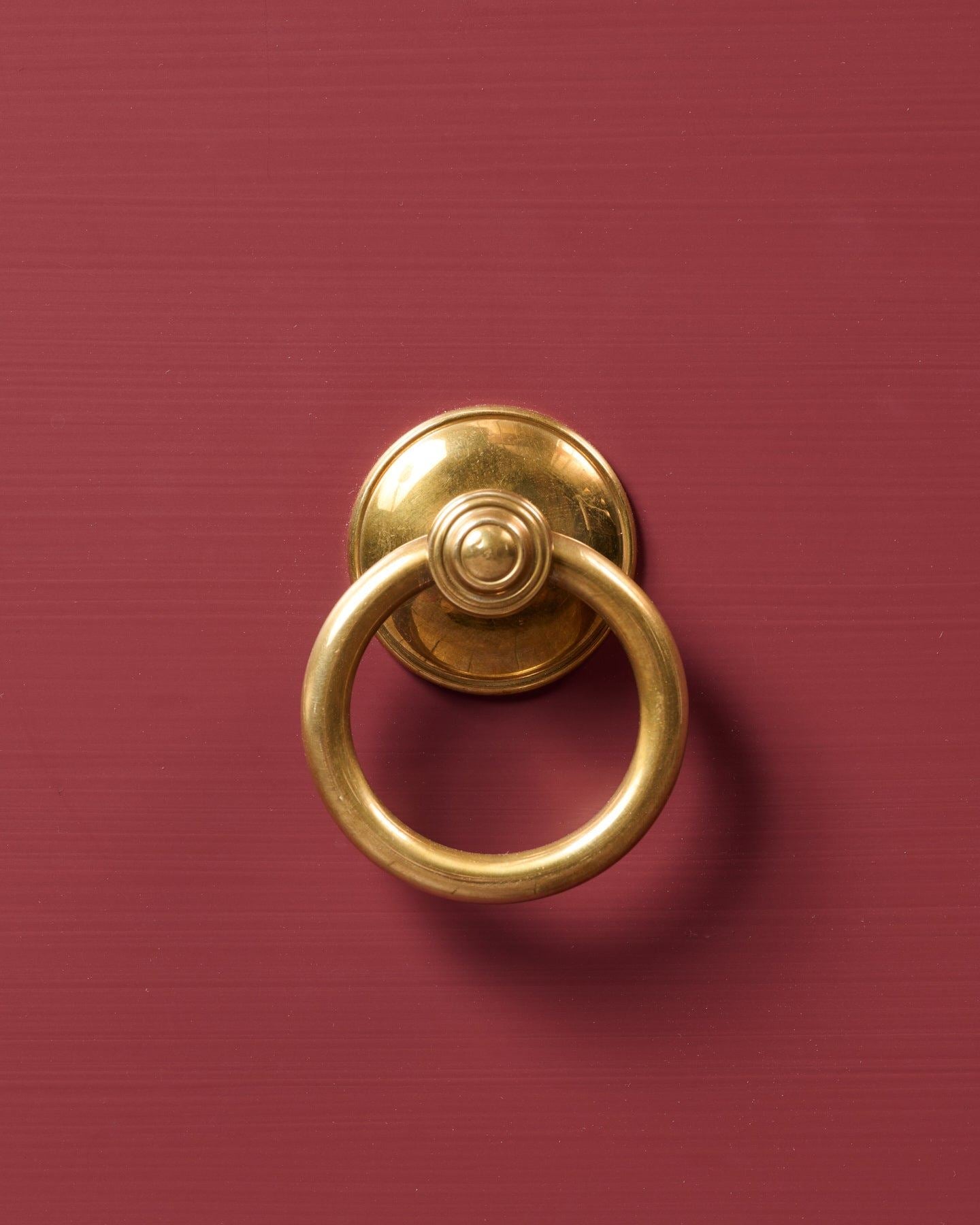 A close-up straight-on view of a Victorian-inspired ring pull handle in a warm burnished brass finish, fitted to a red painted cupboard drawer.