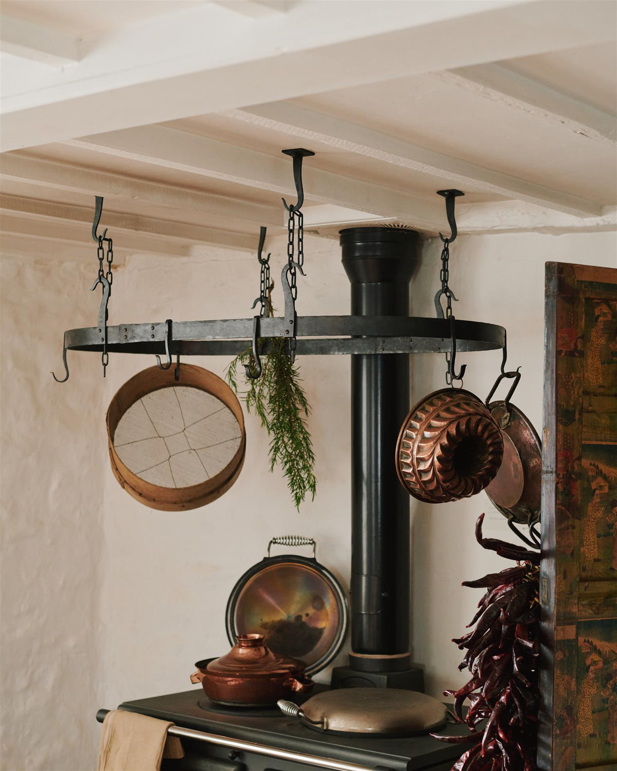 An oblique view of a large oval-shaped wrought iron pot hanger suspended from chains above a black stove cooker. TEST