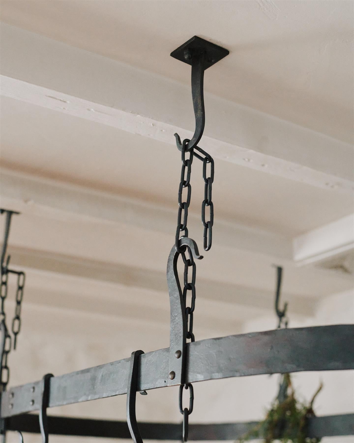 A close-up view of a black chain between the hooks of a wrought iron pot hanger.