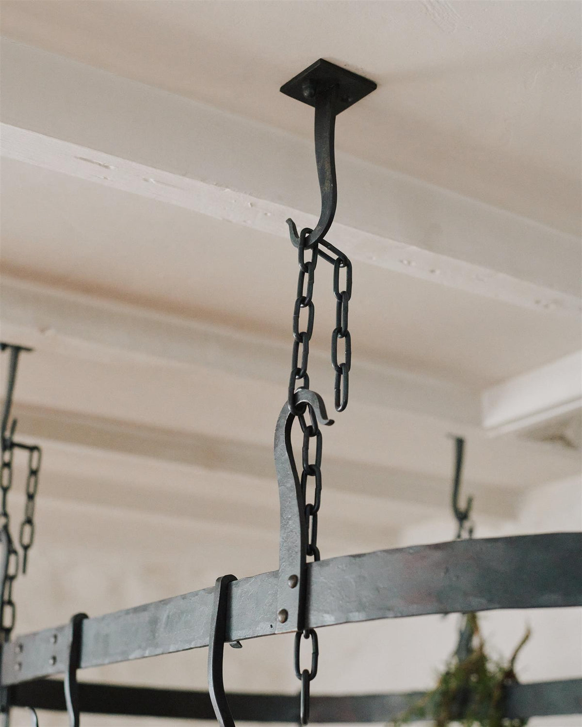 A close-up view of a black chain between the hooks of a wrought iron pot hanger. TEST