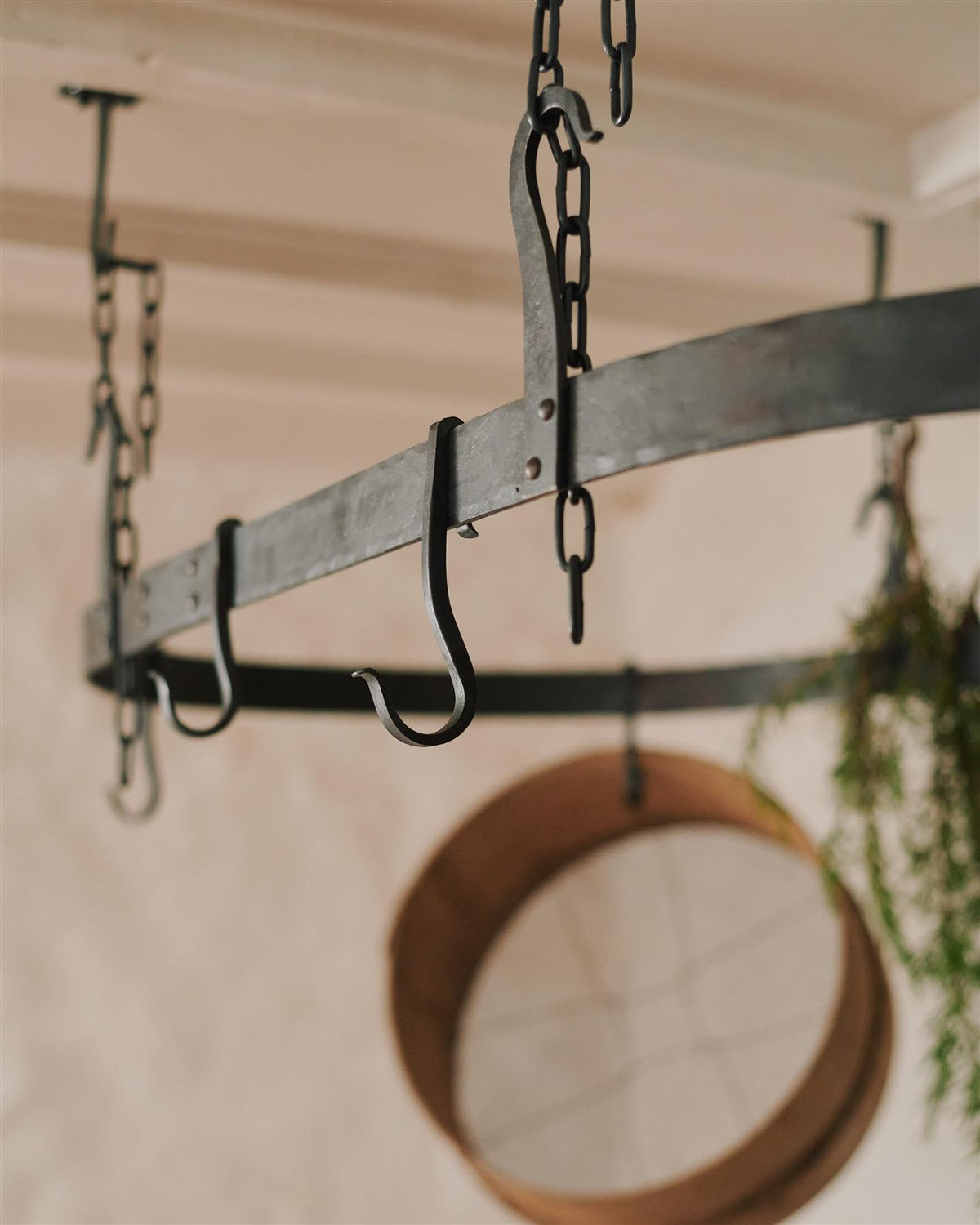 A close-up view of a large oval-shaped wrought iron pot hanger with several looped hooks which hang from the frame. TEST