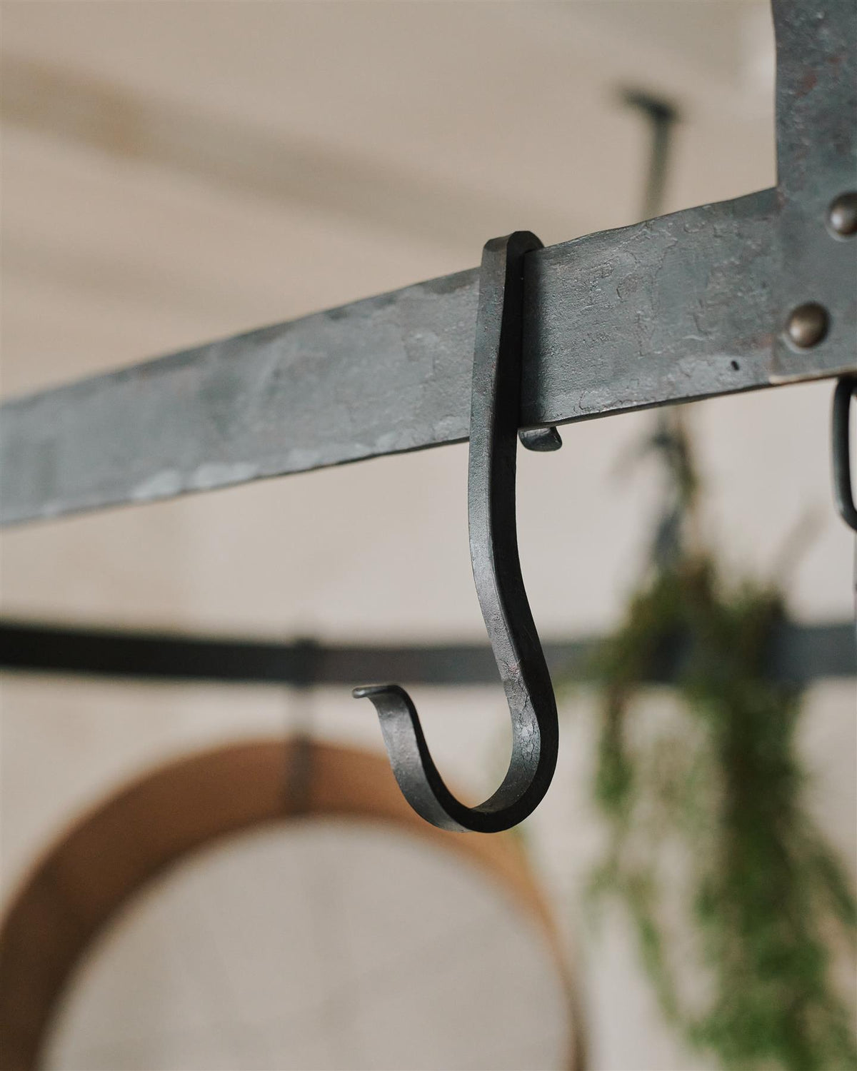 A close-up view of a looped wrought iron hook hanging from the frame of a large oval-shaped pot hanger. TEST