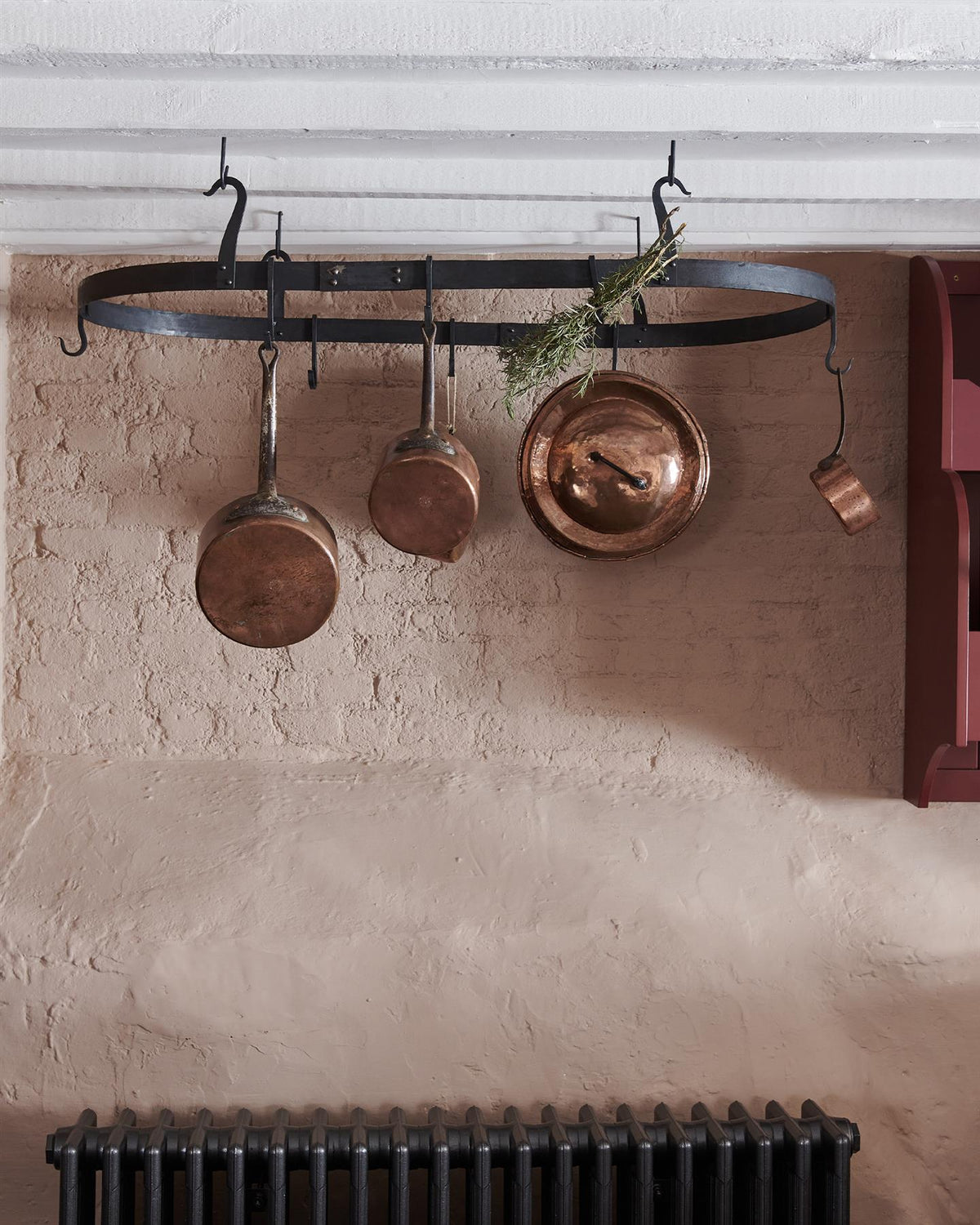 A straight-on view of a large oval-shaped wrought iron pot hanger suspended from a beamed ceiling via iron hooks. TEST