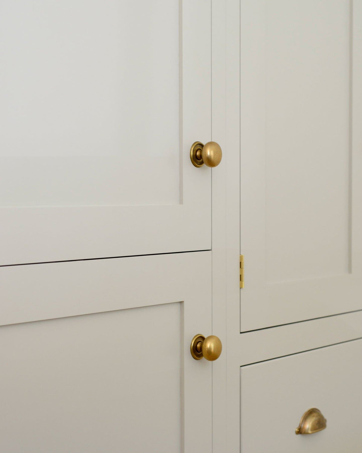 An oblique view of a cream painted Shaker-style pantry cupboard with a set of round doorknobs in a burnished 'Bella' brass finish.|Bella Brass Medium shown TEST