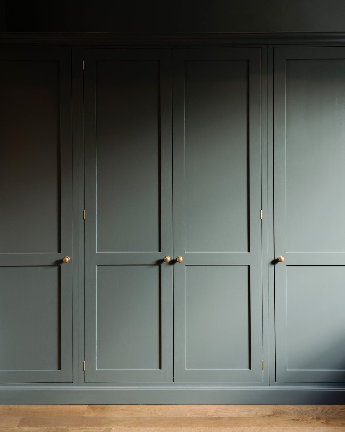 A straight-on view of dark sage green painted Shaker-style full height pantry cupboards, fitted with round doorknobs in a burnished 'Bella' brass finish. TEST