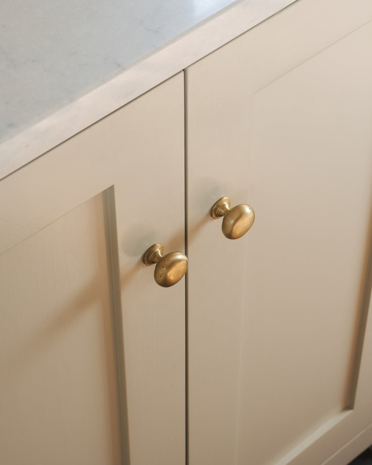 An oblique view of a pair of classic knobs in an aged brass finish, fitted to a mushroom painted Shaker-style kitchen cupboard.|Medium shown TEST
