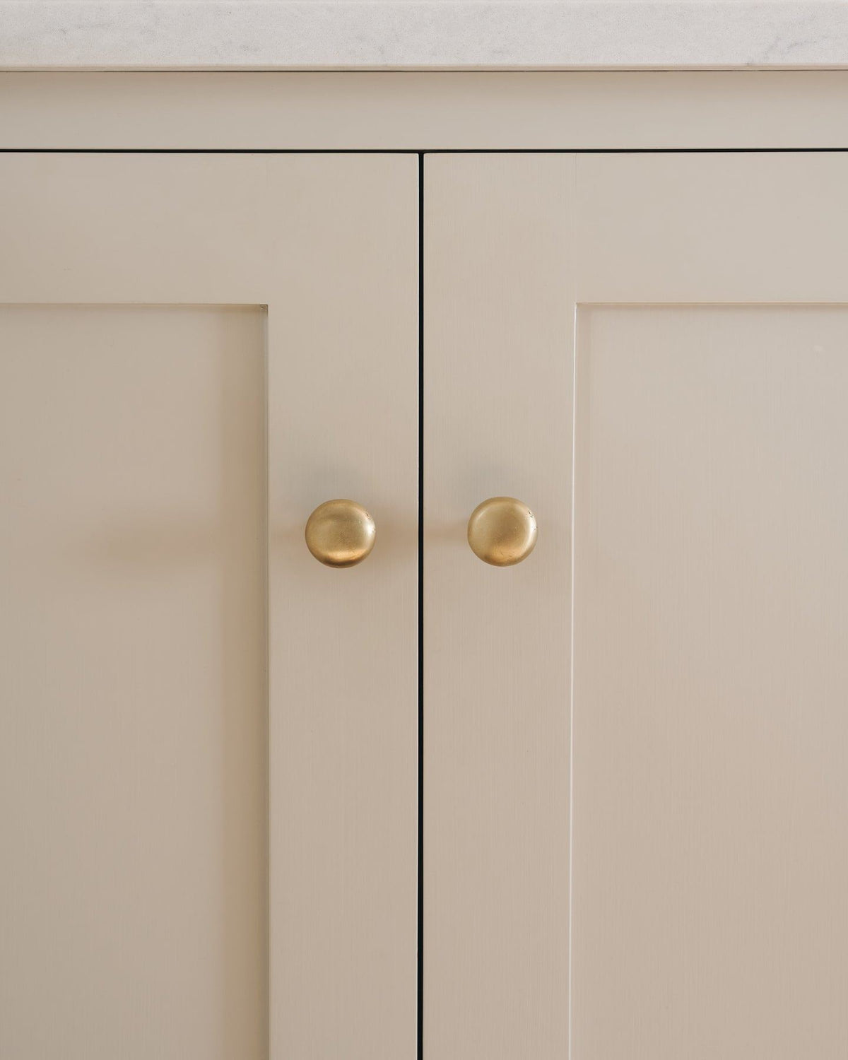 A straight-on view of a pair of classic knobs in an aged brass finish, fitted to a mushroom painted Shaker-style kitchen cupboard.|Medium shown TEST