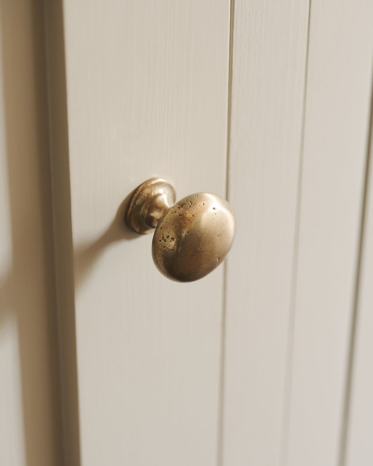 A close-up oblique view of a classic knob in an aged brass finish, fitted to a mushroom painted cupboard door.|Medium shown TEST