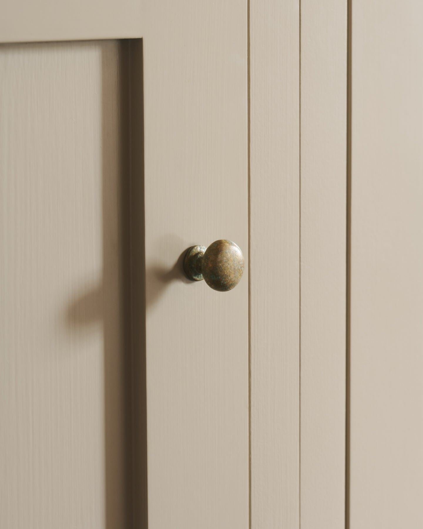 An oblique view of a classic knob in an aged verdrigris brass finish, fitted to a mushroom painted cupboard door.
