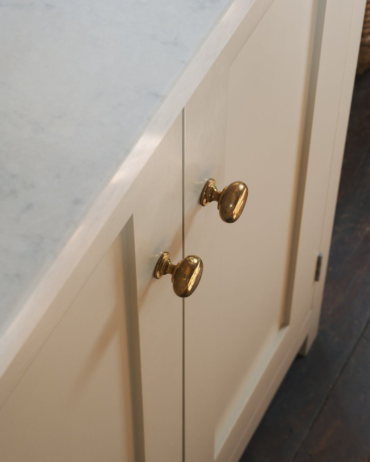 A close-up oblique view of a pair of classic knobs in a warm burnished brass finish, fitted to a mushroom painted Shaker-style kitchen cupboard.|Medium shown TEST