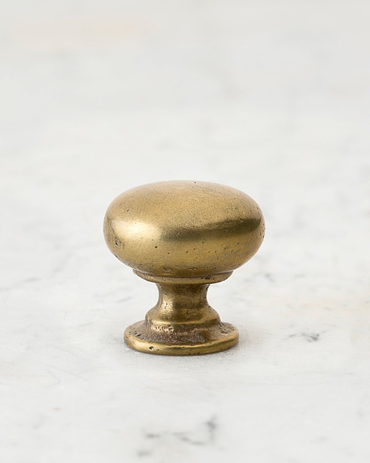 A 'Medium' classic knob for a kitchen cupboard or drawer with an aged brass finish and unique dented textures that makes it look like a beloved, well aged brass from centuries ago.