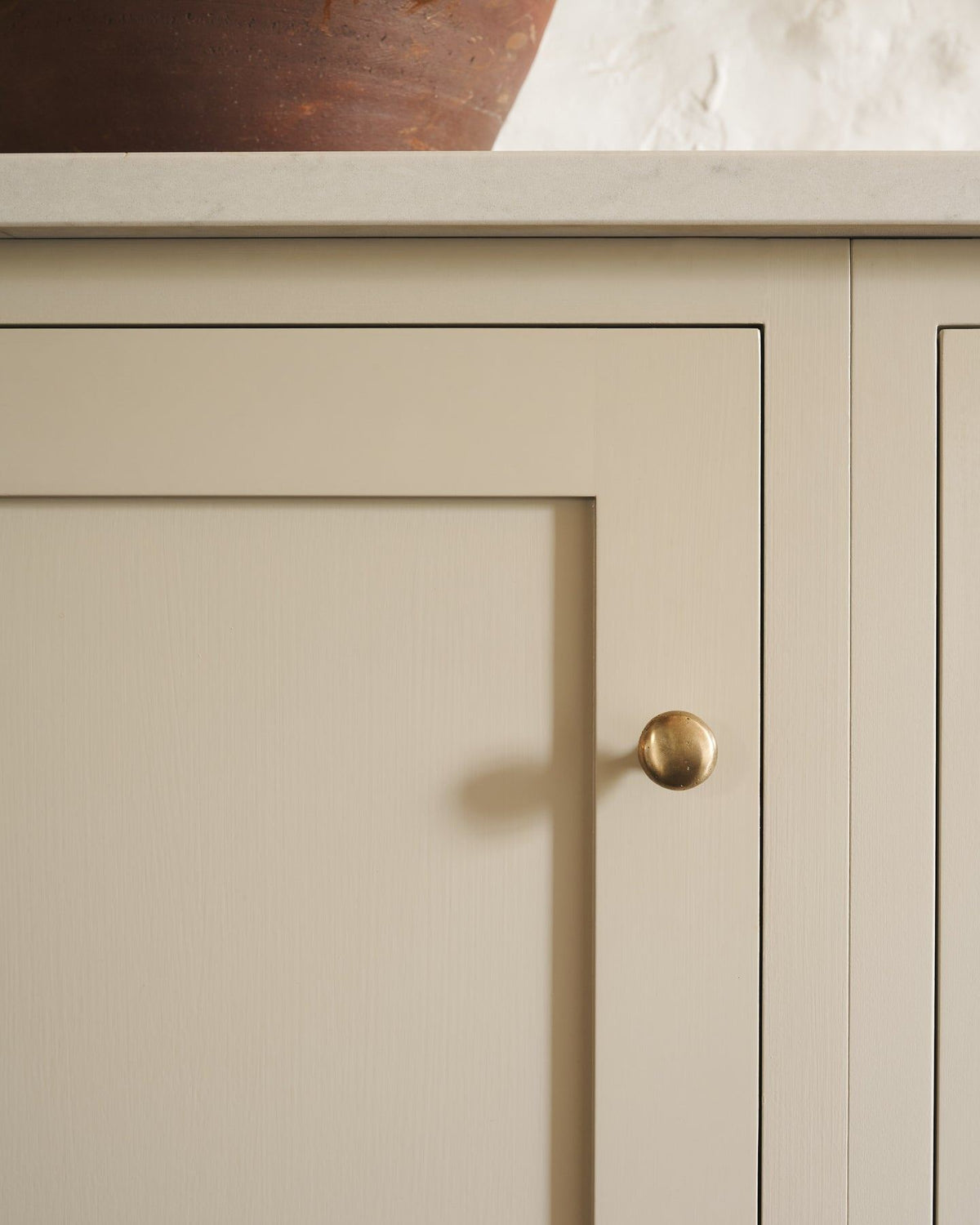 A straight-on view of a classic knob in an aged brass finish, fitted to a mushroom painted cupboard door. TEST