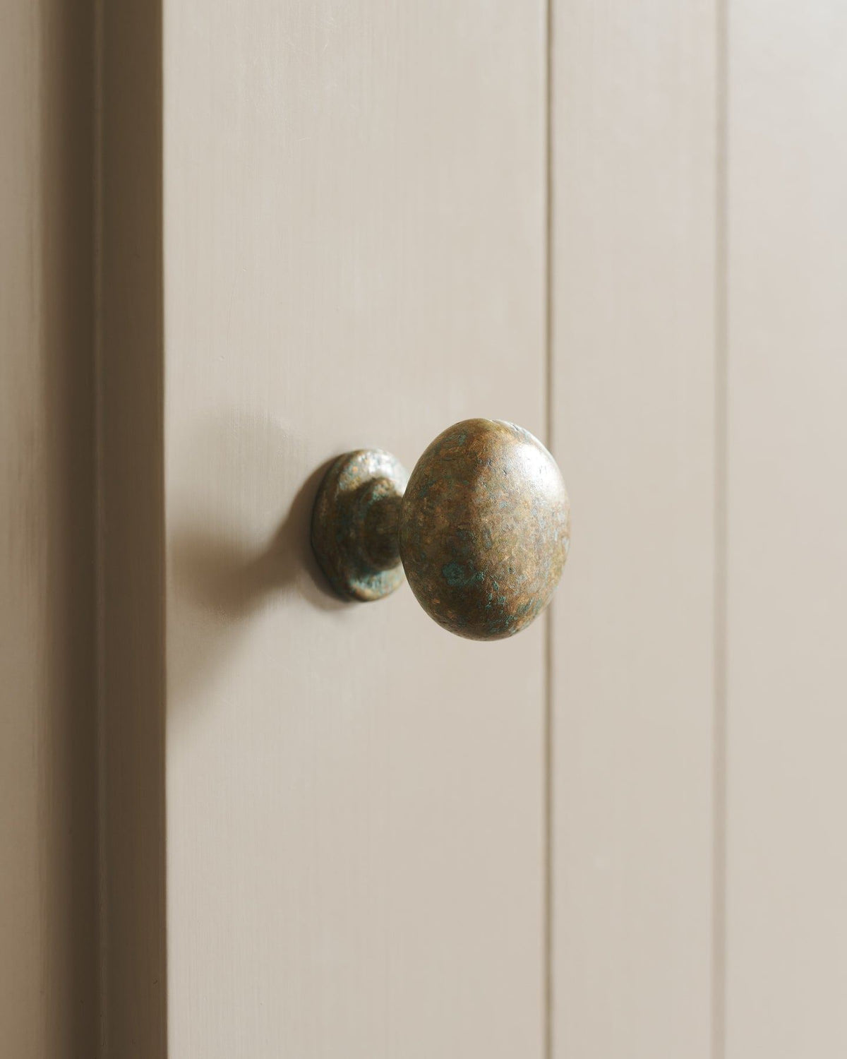 A close-up oblique view of a classic knob in an aged verdrigris brass finish, fitted to a mushroom painted cupboard door. TEST