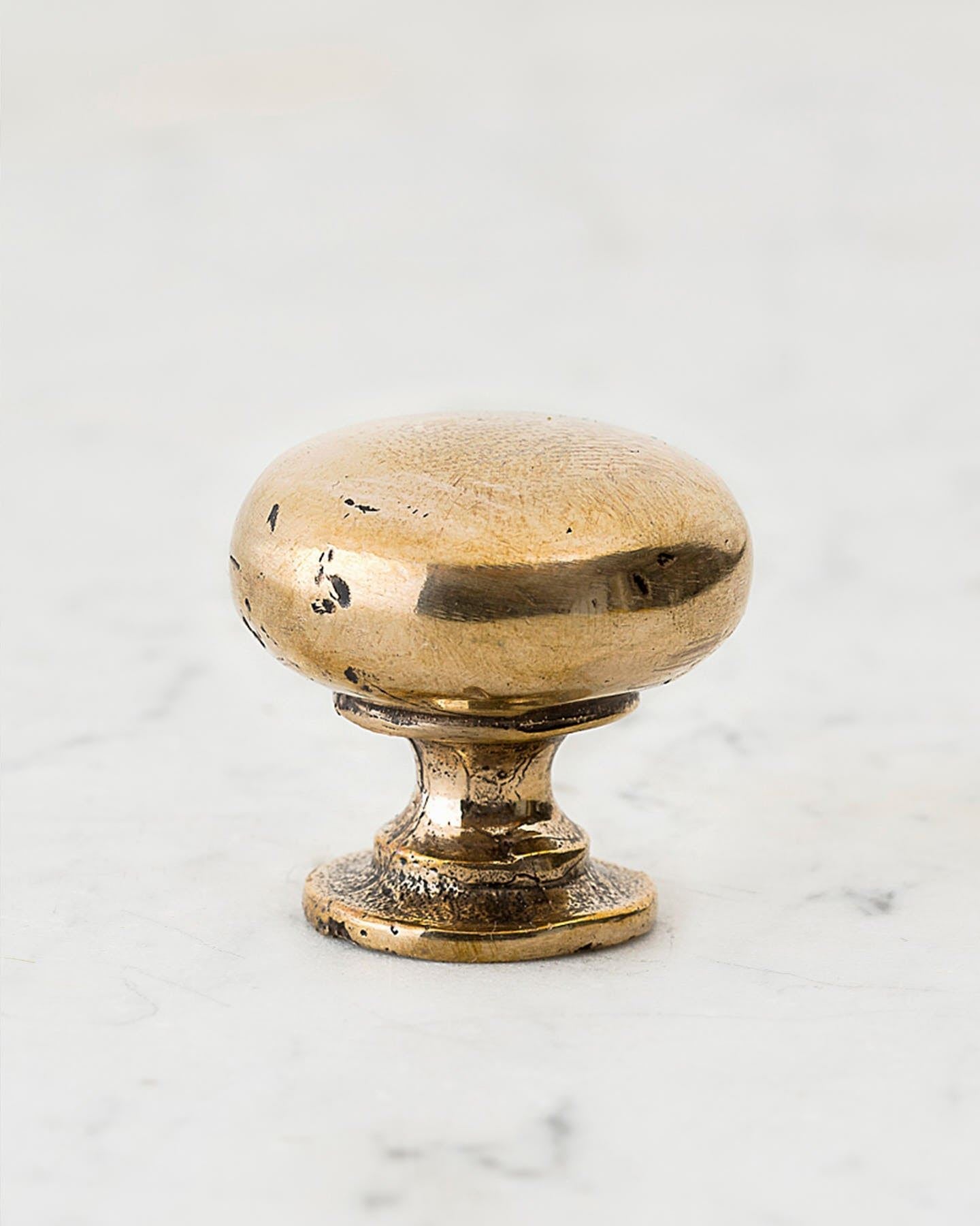A 'Large' classic knob for a kitchen cupboard or drawer with a bright polished bronze finish and unique dented textures that makes it look like a beloved, well aged bronze from centuries ago.