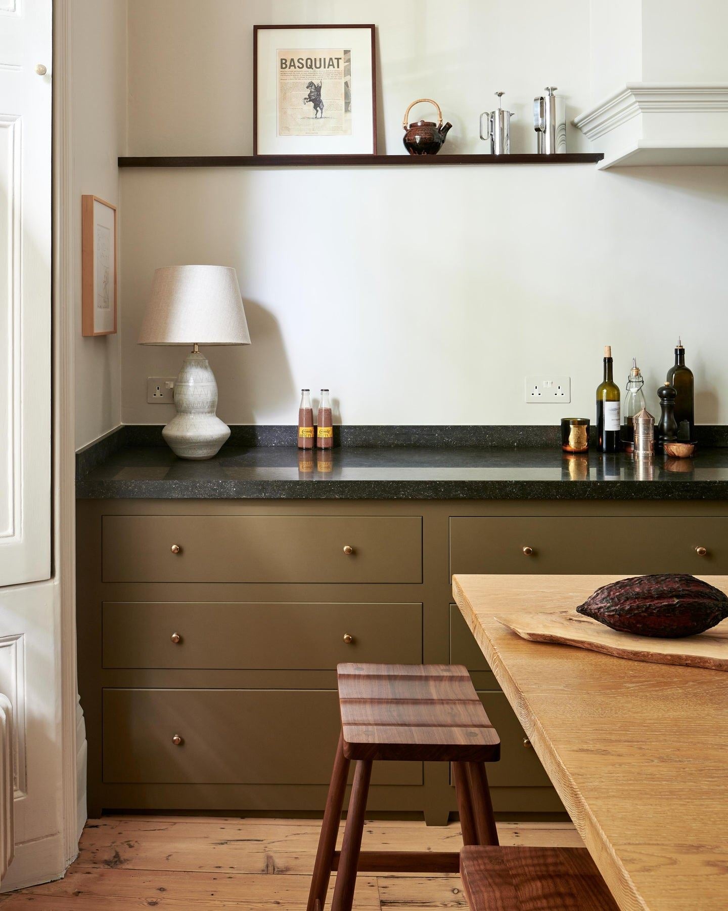 A straight-on view of a mossy green painted Georgian-style kitchen with rows of pan drawers fitted with classic knobs in a bright polished bronze finish.