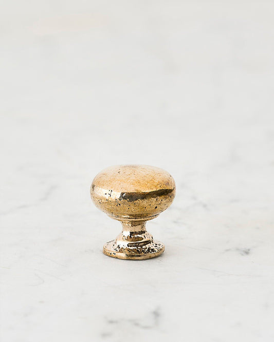 A 'Petite' classic knob for a kitchen cupboard or drawer with a bright polished bronze finish and unique dented textures that makes it look like a beloved, well aged bronze from centuries ago.