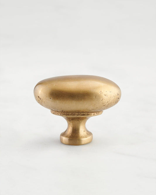A 'Medium' oval-shaped knob for a kitchen cupboard or drawer with an aged brass finish and unique dented textures that makes it look like a beloved, well aged brass from centuries ago.