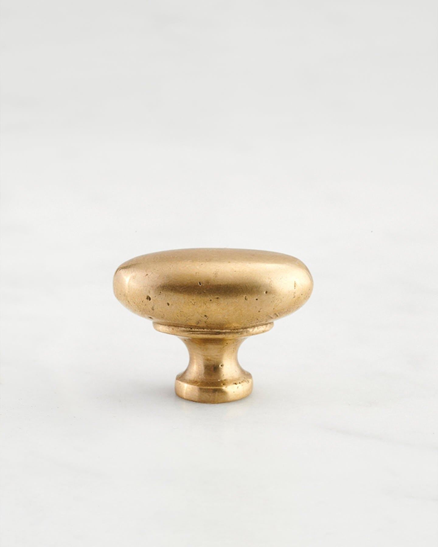 A 'Small' oval-shaped knob for a kitchen cupboard or drawer with an aged brass finish and unique dented textures that makes it look like a beloved, well aged brass from centuries ago.