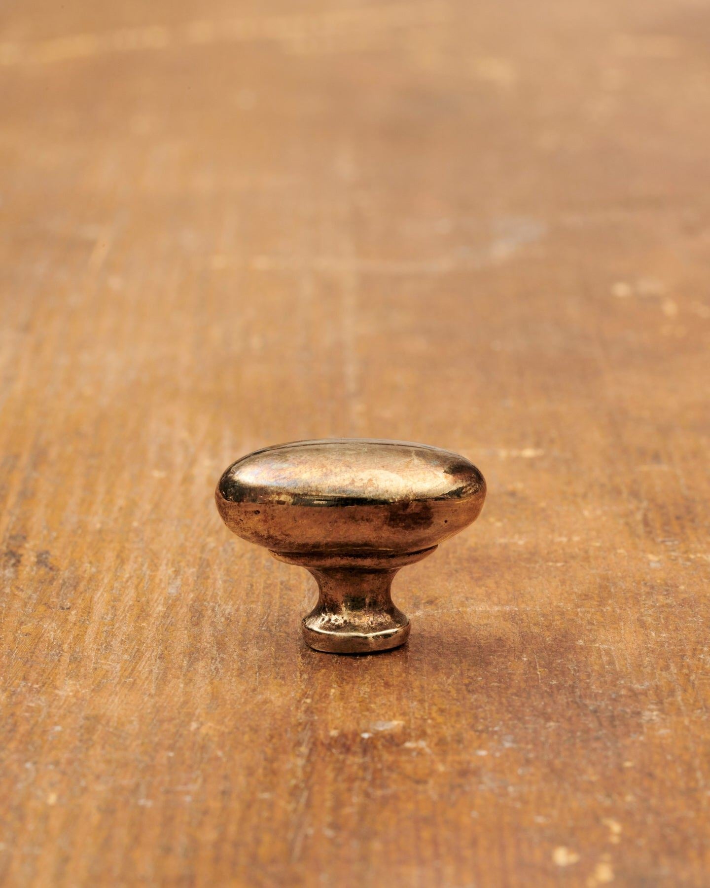 A 'Petite' oval-shaped knob for a kitchen cupboard or drawer with a warm burnished brass finish and unique dented textures as if was made by an artisan blacksmith centuries ago.