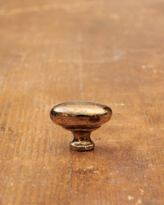A 'Petite' oval-shaped knob for a kitchen cupboard or drawer with a warm burnished brass finish and unique dented textures as if was made by an artisan blacksmith centuries ago.