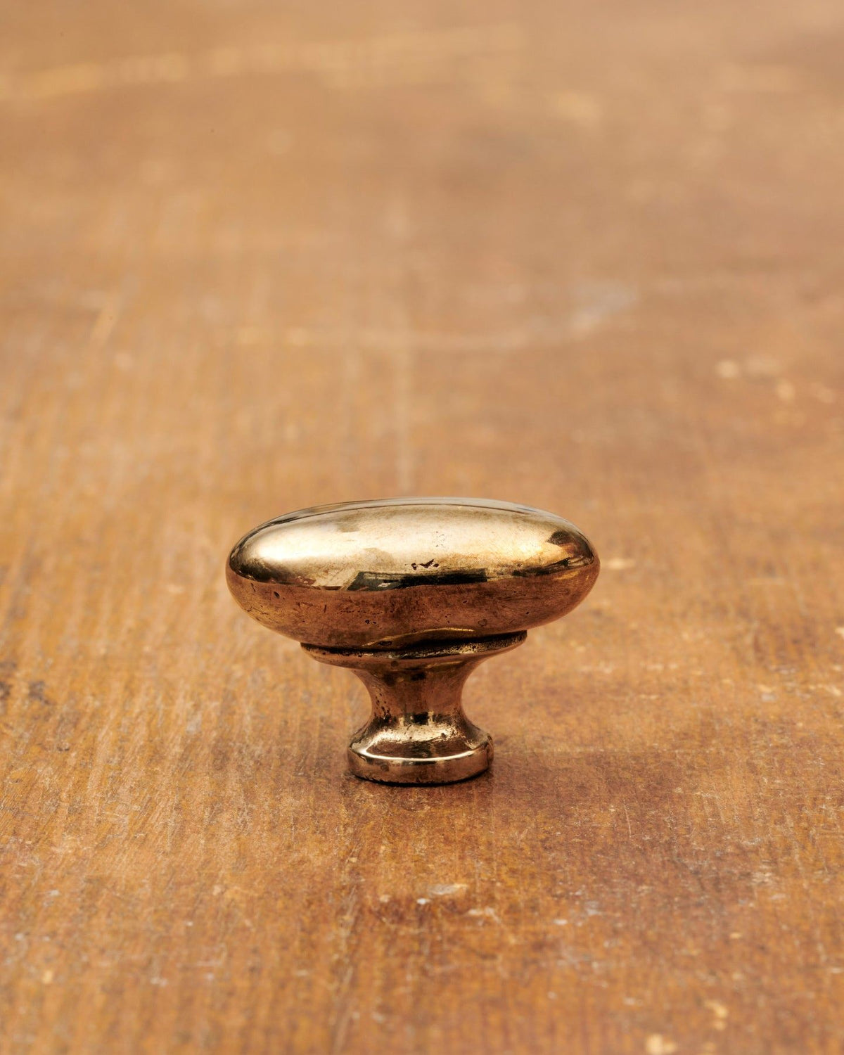 A 'Small' oval-shaped knob for a kitchen cupboard or drawer with a warm burnished brass finish and unique dented textures as if was made by an artisan blacksmith centuries ago. TEST