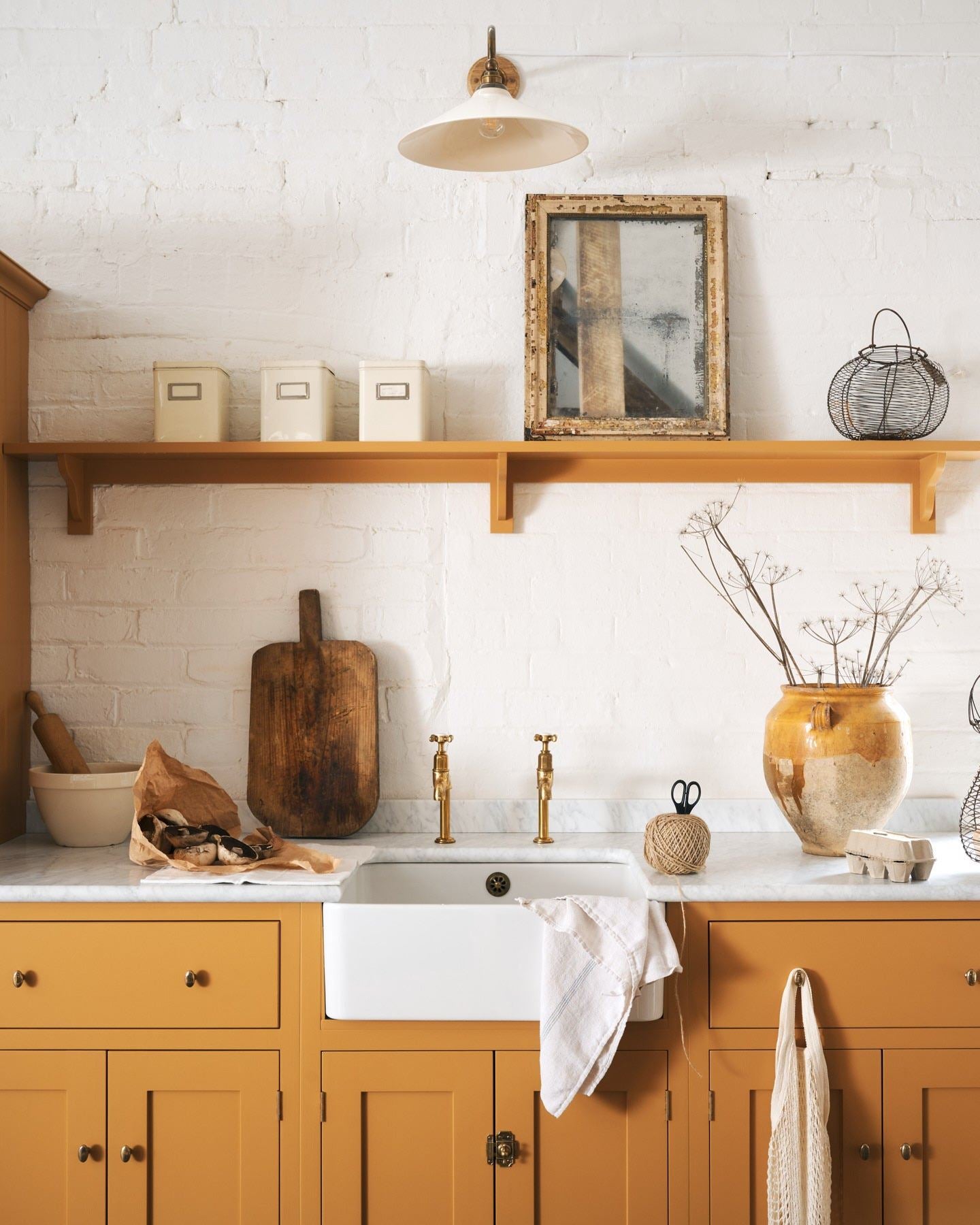 A straight-on view of a yellow painted Shaker-style kitchen sink cupboard with small oval-shaped knobs in a warm burnished brass finish.