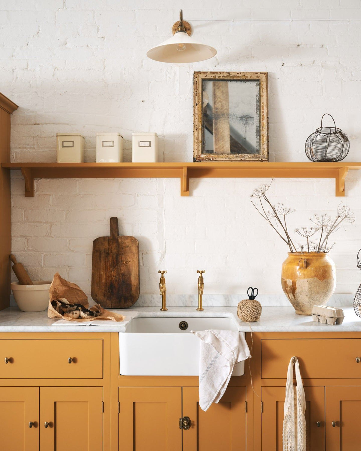 A straight-on view of a yellow painted Shaker-style kitchen sink cupboard with small oval-shaped knobs in a warm burnished brass finish.|Small shown TEST