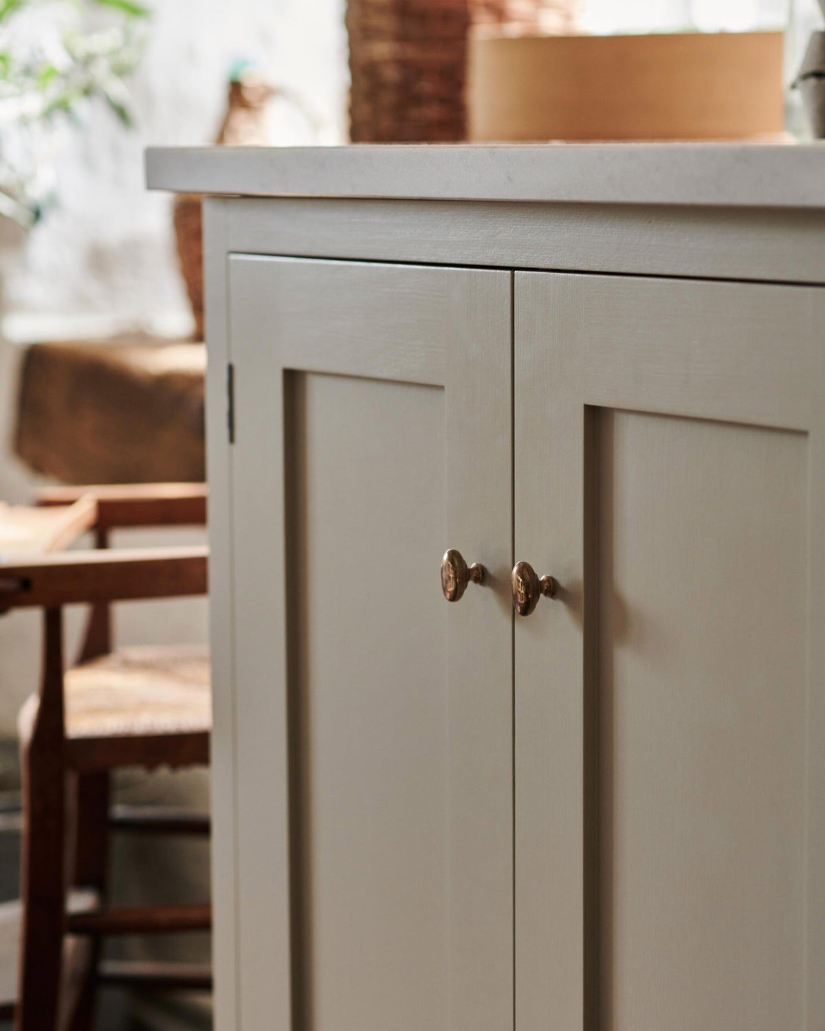 An oblique view of a pair of oval-shaped knobs in a warm burnished brass finish, fitted to a mushroom painted Shaker-style kitchen cupboard.|Heirloom Brass Small shown TEST