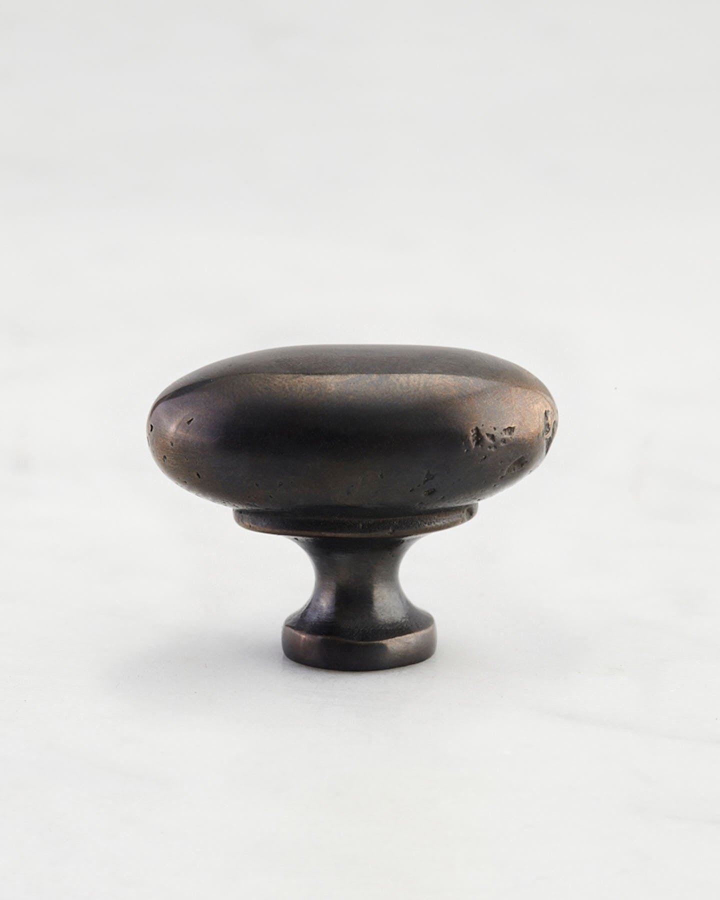 A 'Medium' oval-shaped knob for a kitchen cupboard or drawer with a dark oxidised bronze finish and unique dented textures as if was made by an artisan blacksmith centuries ago.