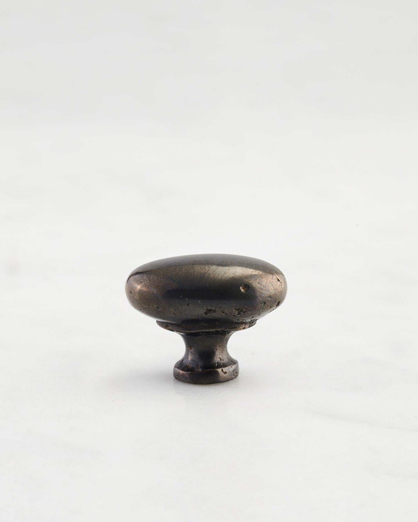 A 'Petite' oval-shaped knob for a kitchen cupboard or drawer with a dark oxidised bronze finish that makes it look like a beloved, well aged brass from centuries ago.
