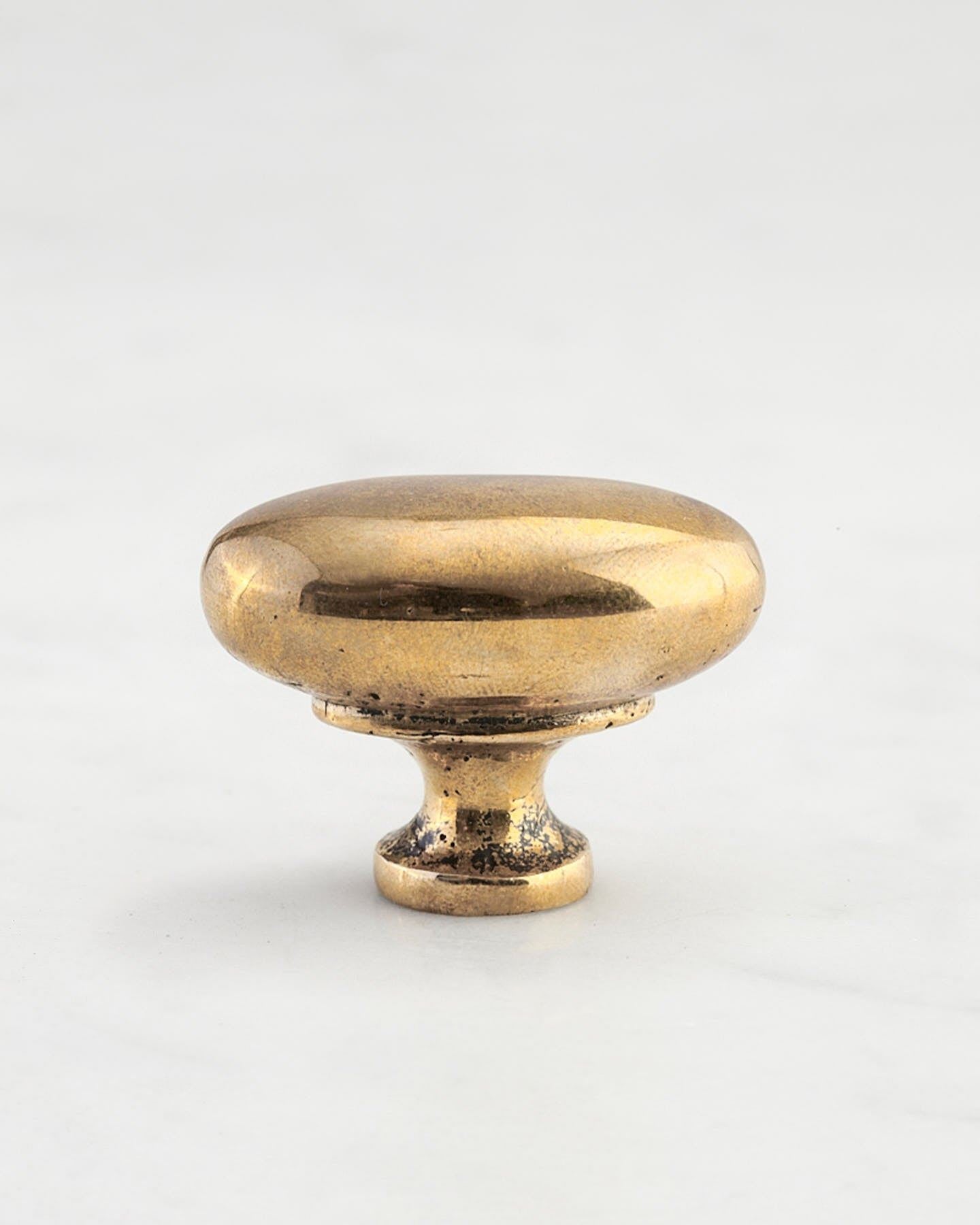 A 'Medium' oval-shaped knob for a kitchen cupboard or drawer with a bright polished bronze finish and unique dented textures that makes it look like a beloved, well aged bronze from centuries ago.
