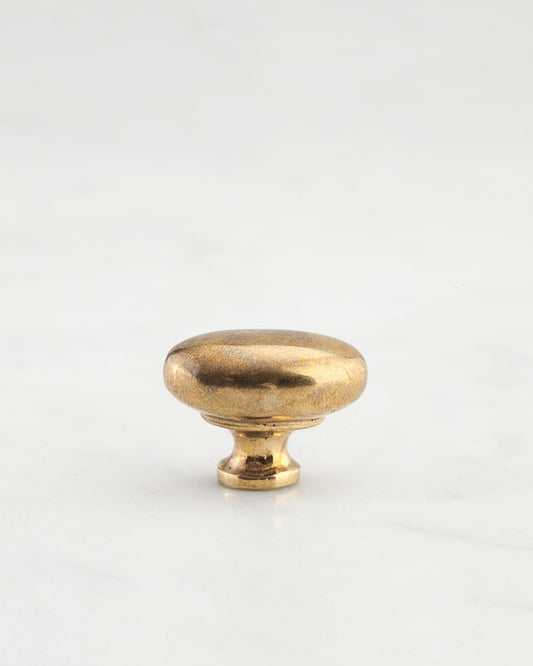 A 'Petite' oval-shaped knob for a kitchen cupboard or drawer with a bright polished bronze finish and unique dented textures that makes it look like a beloved, well aged bronze from centuries ago.