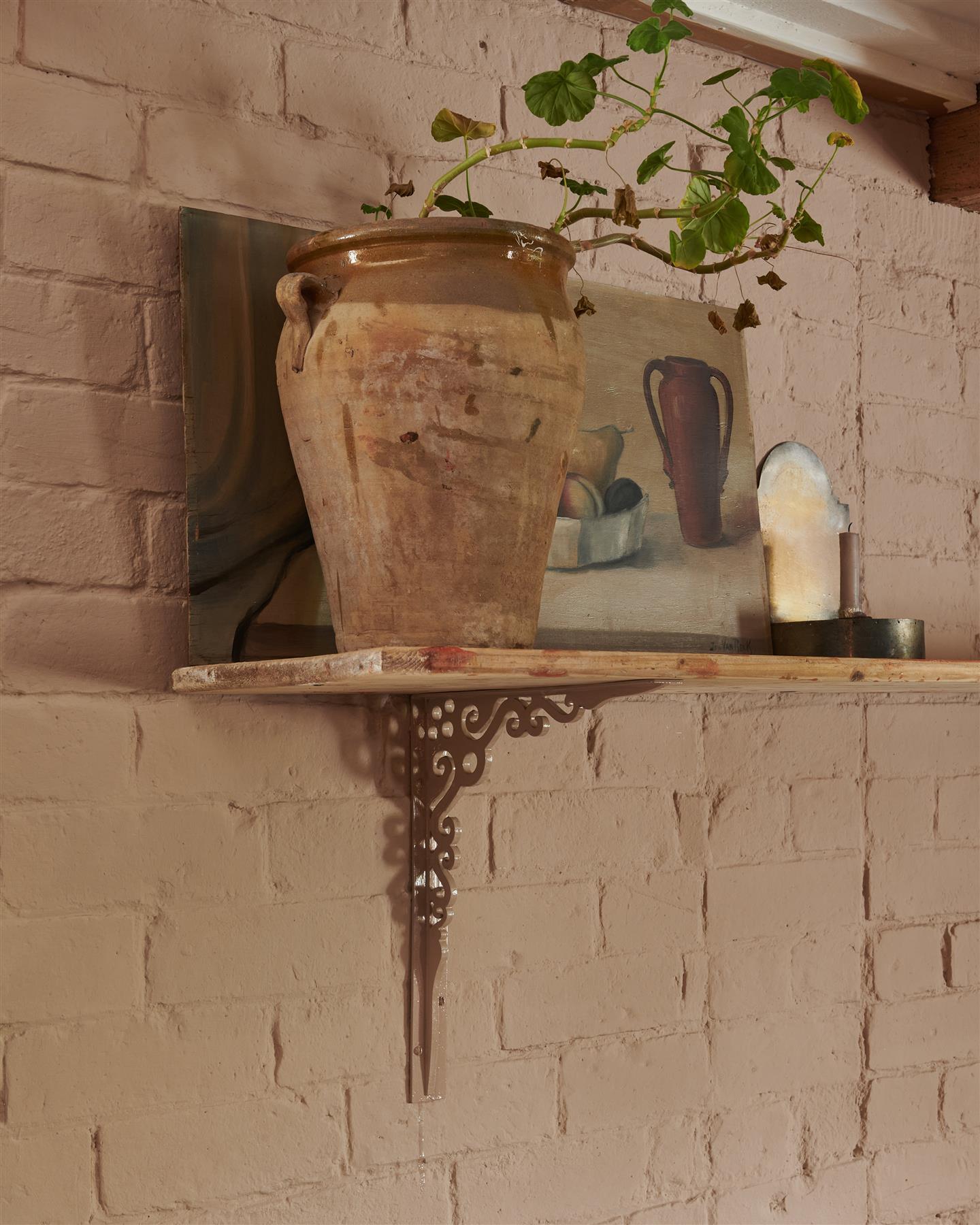 An oblique view of a large Victorian-inspired ornate pink painted shelf bracket holding a deep pine shelf to a pink colour brick wall.