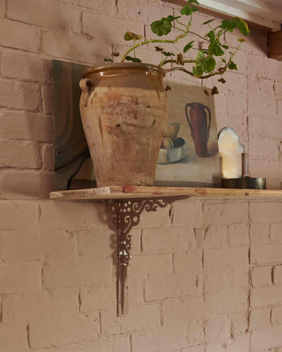 An oblique view of a large Victorian-inspired ornate pink painted shelf bracket holding a deep pine shelf to a pink colour brick wall. | Aged Brass Large shown TEST