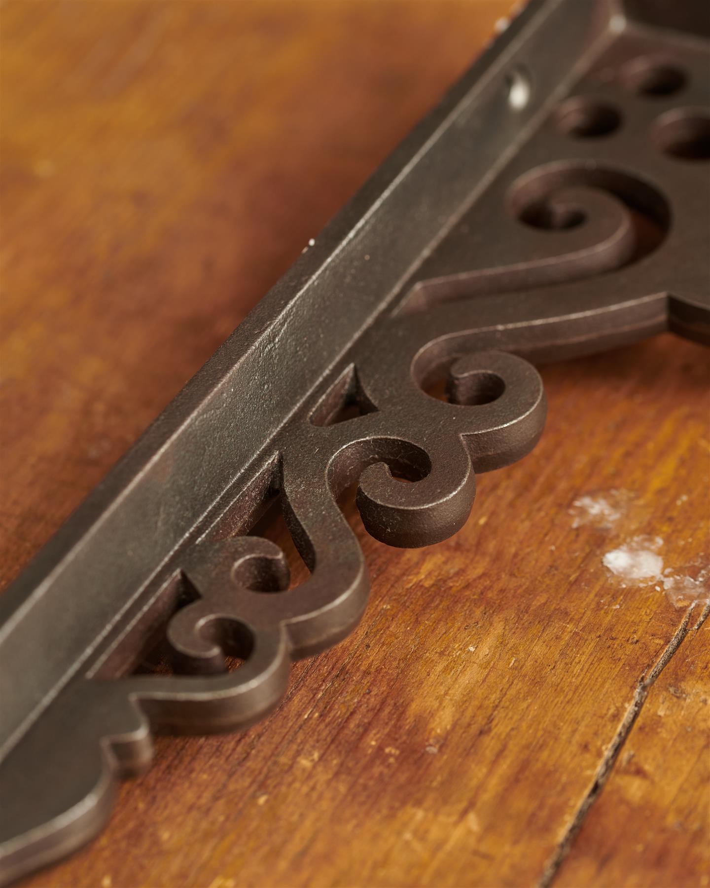 A close-up view of the decorative cutout patterns on a large Victorian-inspired ornate cast iron shelf bracket.