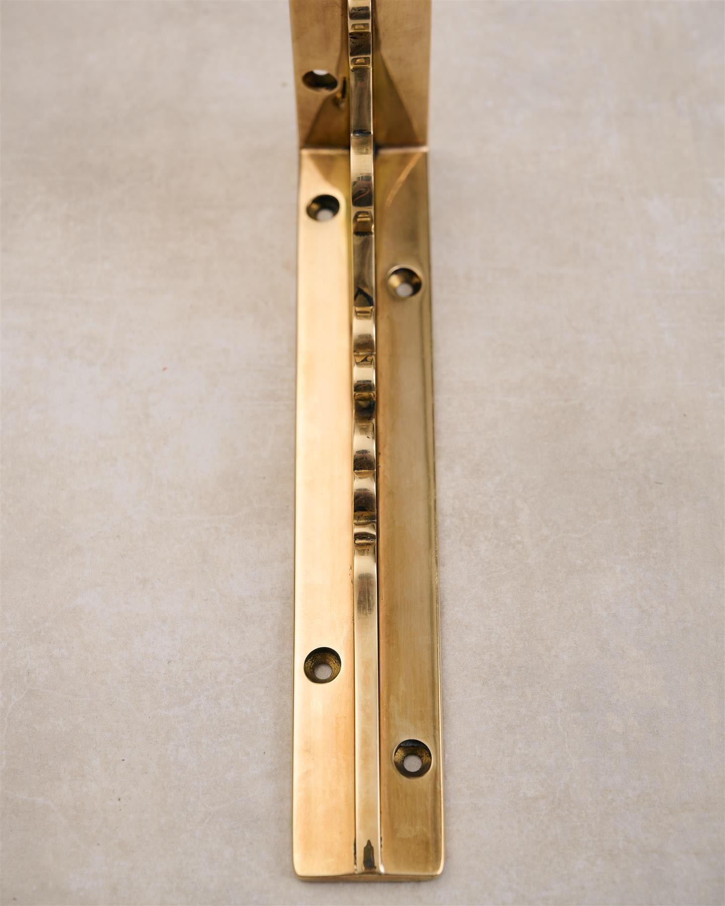 A close-up front profile view of a small Victorian-inspired ornate shelf bracket in a warm polished brass finish.