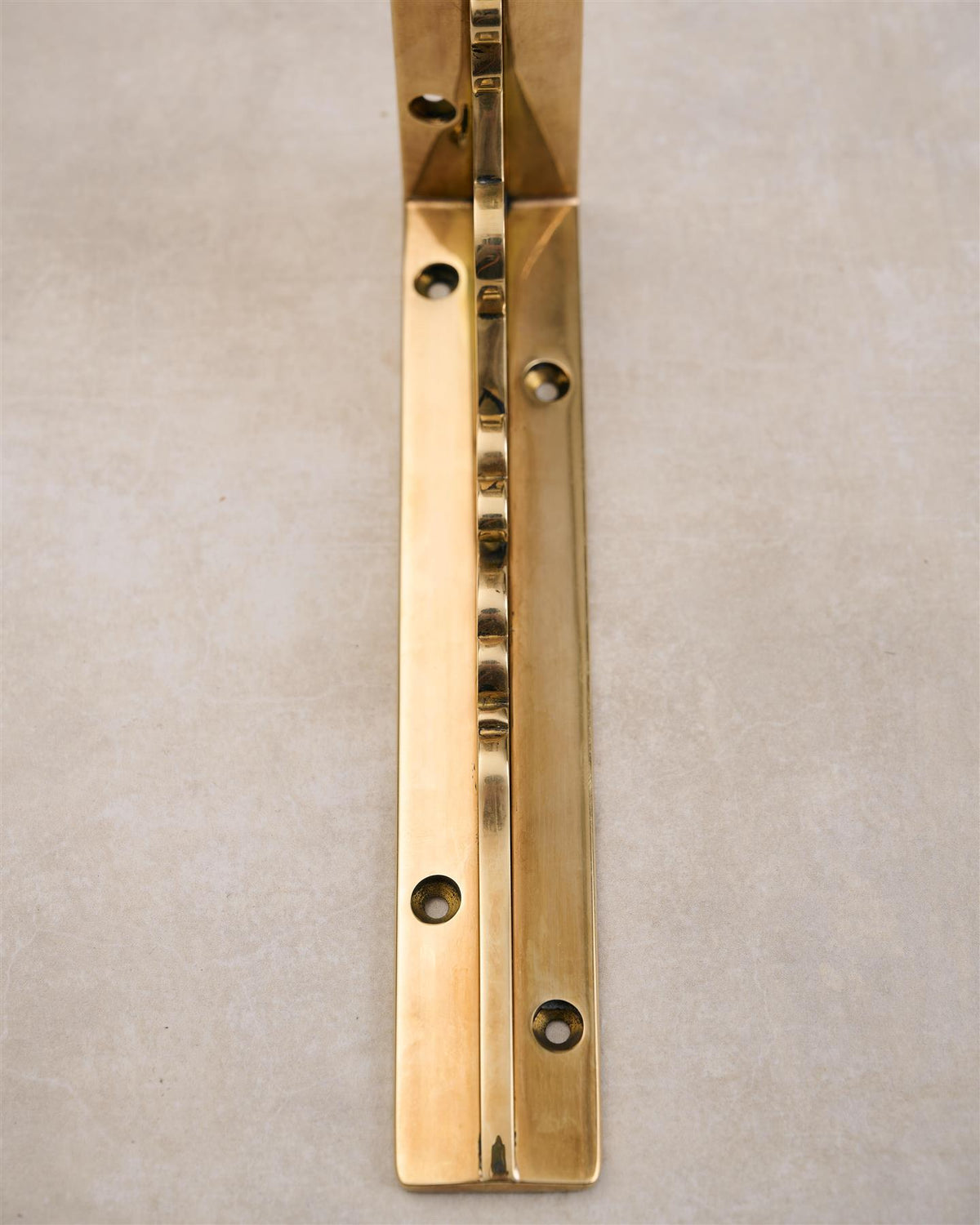 A close-up front profile view of a small Victorian-inspired ornate shelf bracket in a warm polished brass finish. TEST