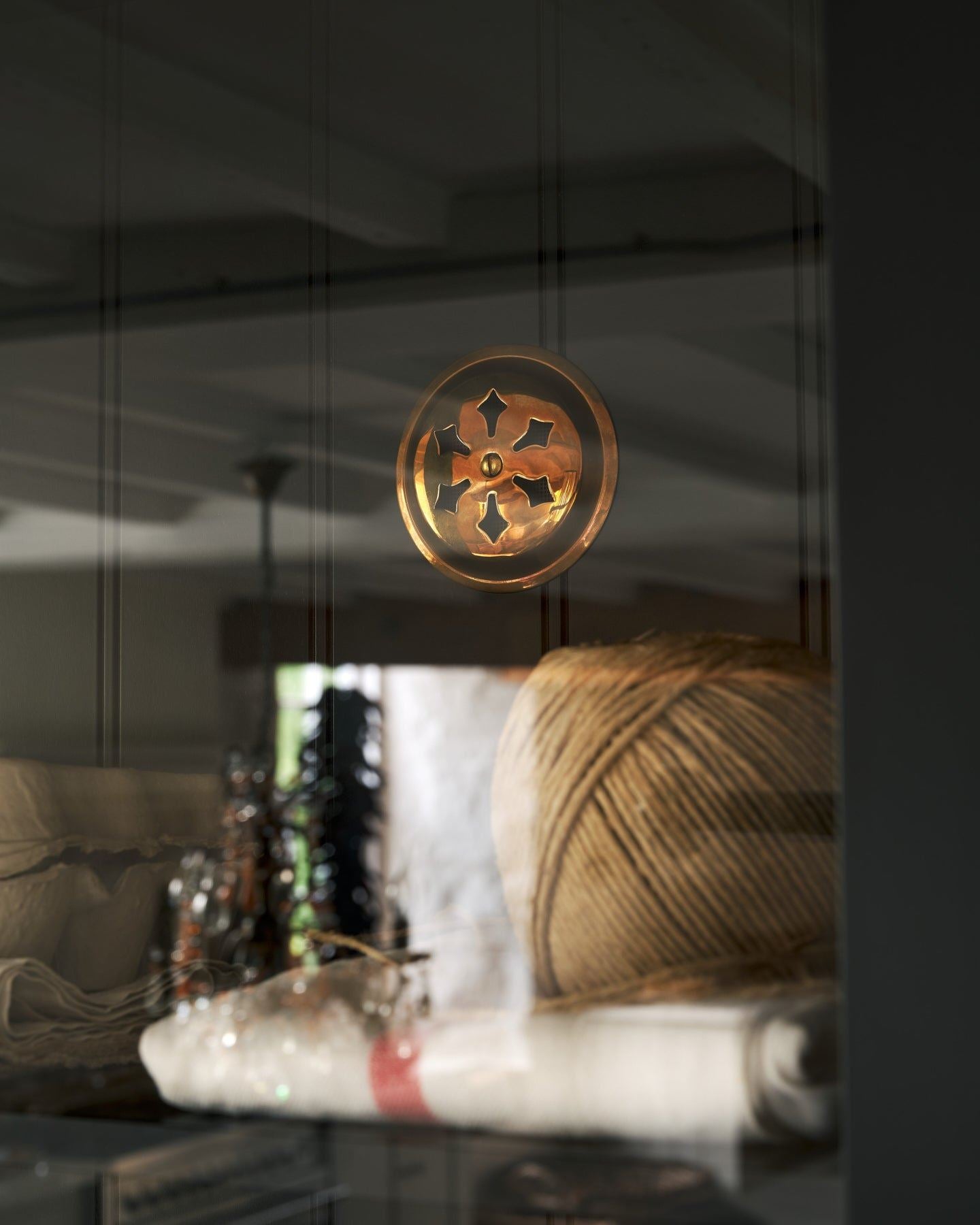 Looking through a glazed cupboard door at a Victorian-inspired circular brass ventilation grille with traditional decorative cutouts fitted to a black painted tongue and groove-style back panel.