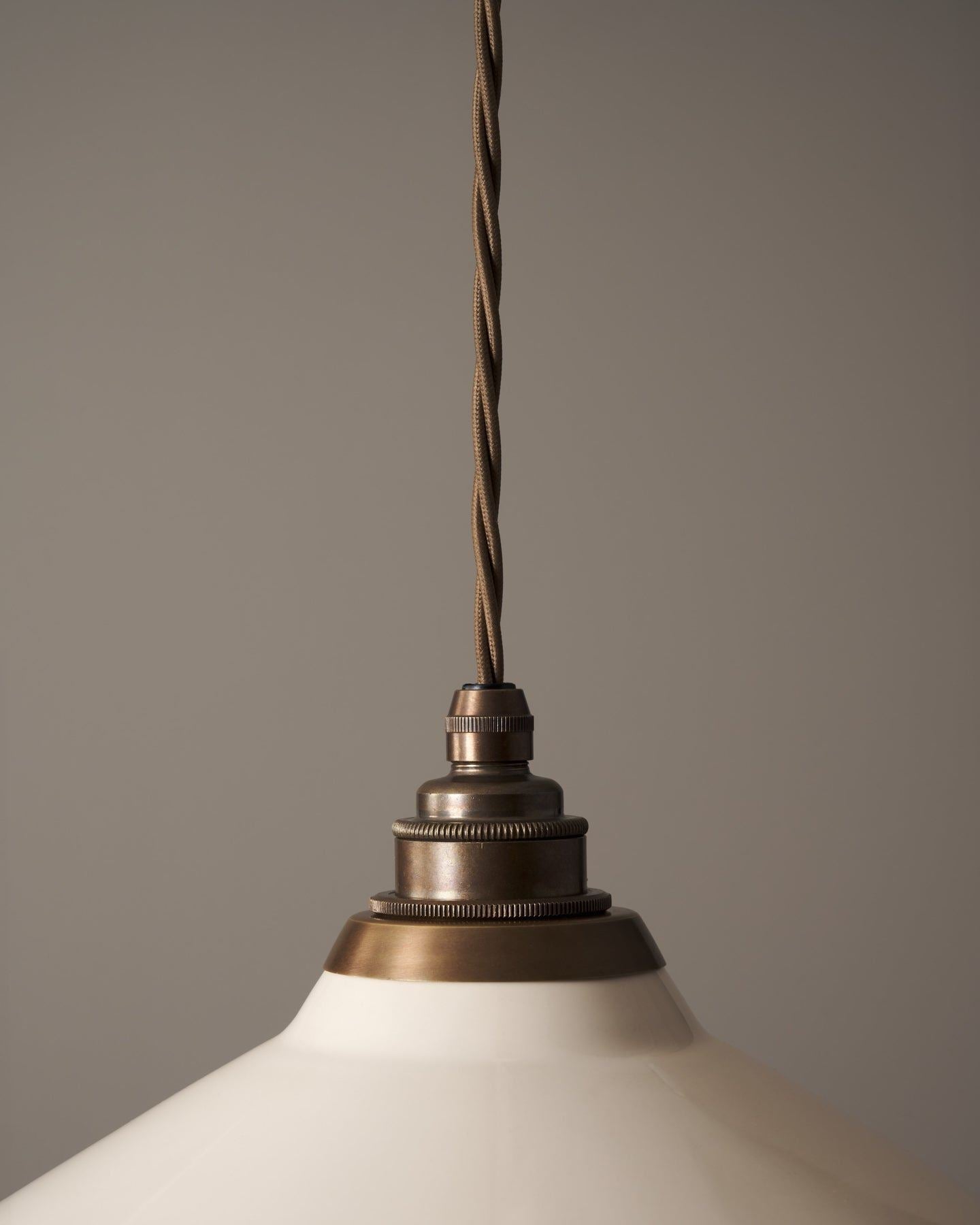 A close-up view of an aged brass E27 lampholder attached to a cream glazed ceramic light shade.