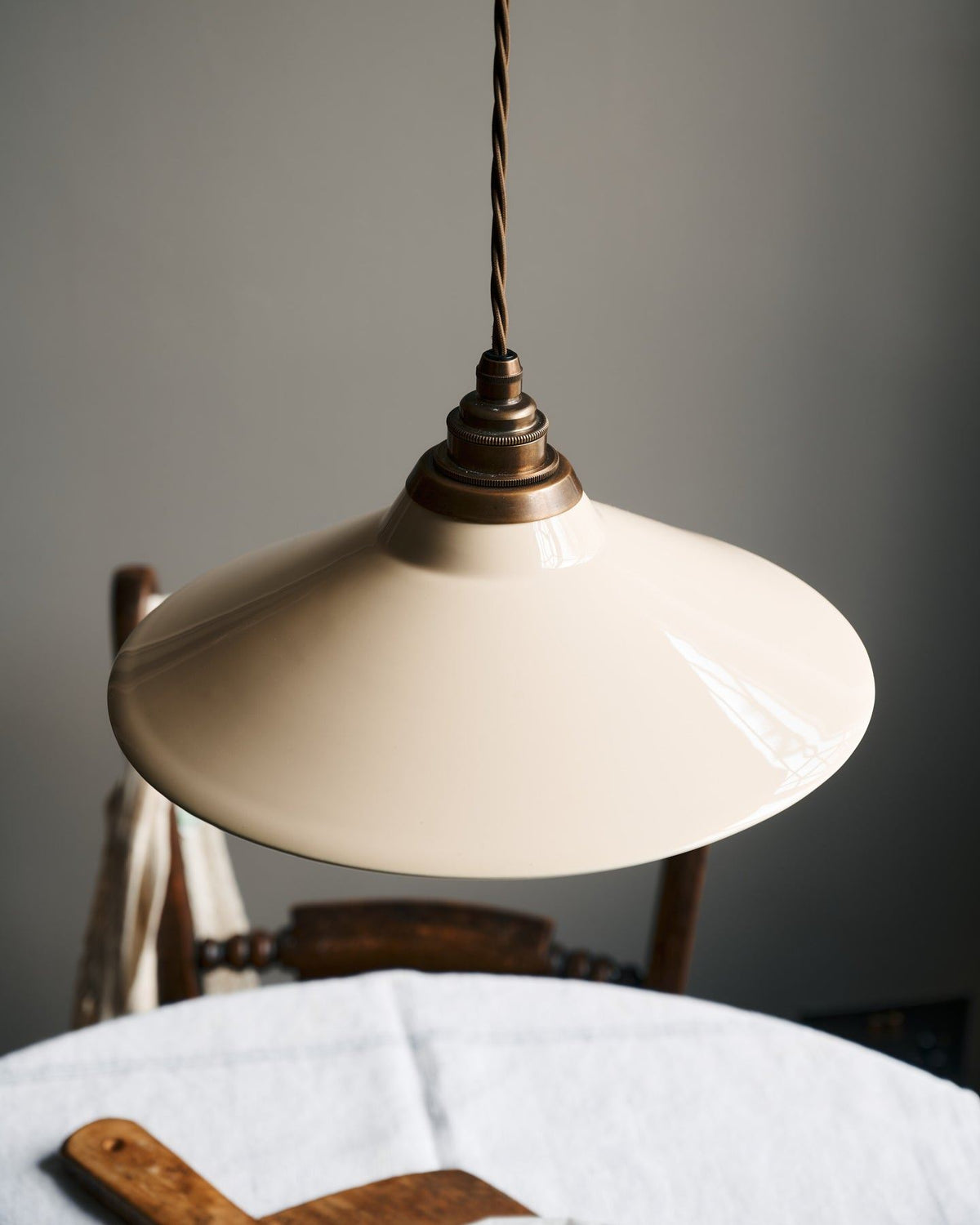 A close-up view of a small cream glazed ceramic shade with aged brass fittings and brown twisted fabric flex cord. TEST