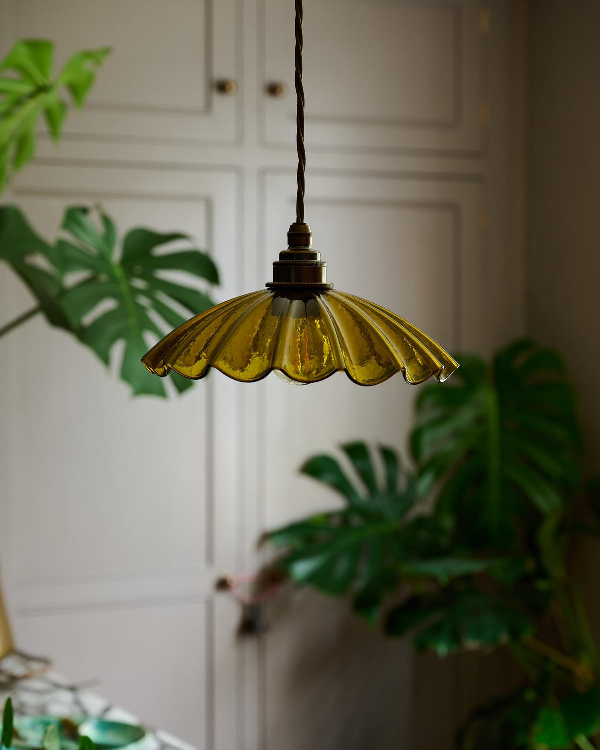 A small frilly chartreuse glass pendant light with brass fittings and brown twisted fabric flex cord. The light is off. TEST