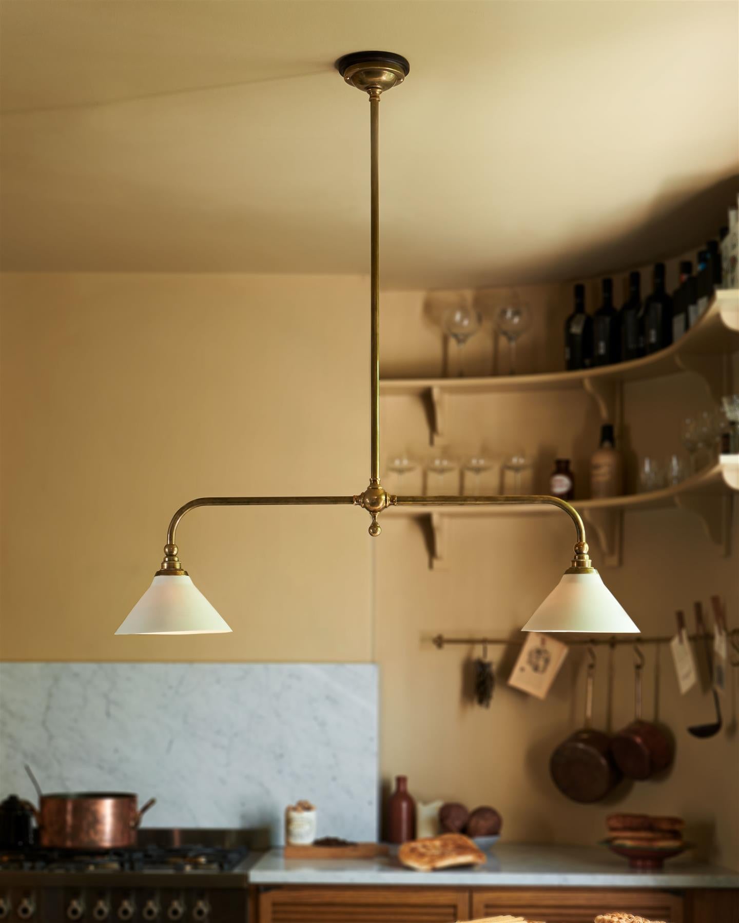A straight-on view of a mid-century-style kitchen with oak cabinetry, buttery yellow walls and a Victorian-inspired chandelier light with brass arms and small unglazed porcelain shades over a prep table with a Carrara marble worktop.