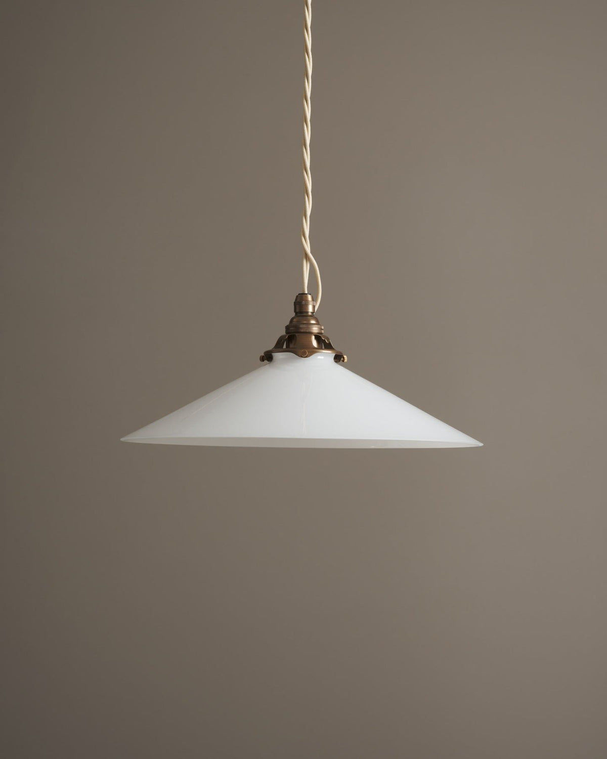 A classic pendant light with a milk glass light shade, an aged brass E27 lampholder with a decorative gallery and cream twisted fabric flex cord. The light is off. TEST