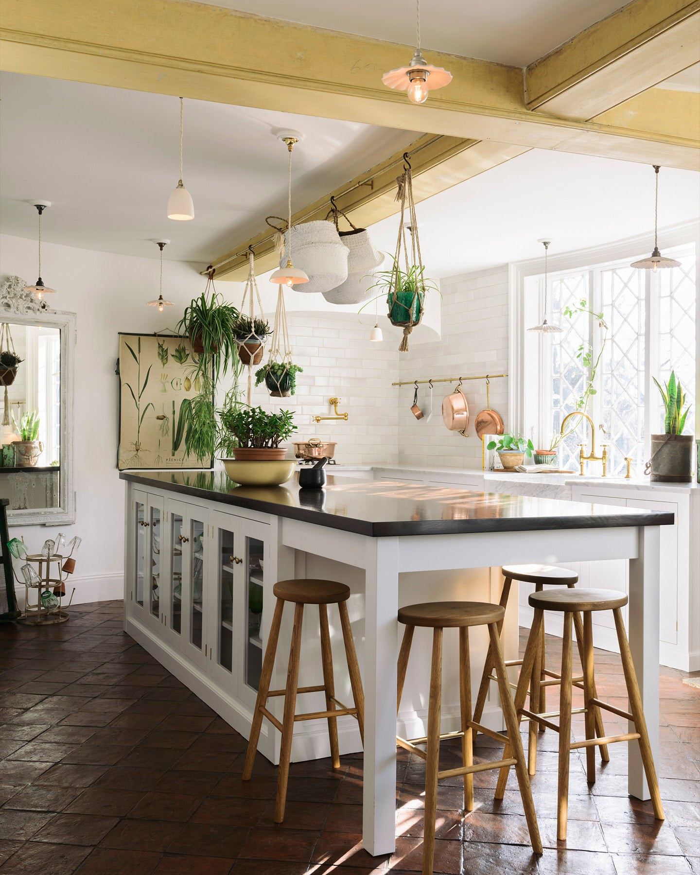 A Mediterranean-style kitchen with white painted cabinetry, white walls, terracotta flooring and an assortment of unglazed porcelain pendant lights hanging at various heights.