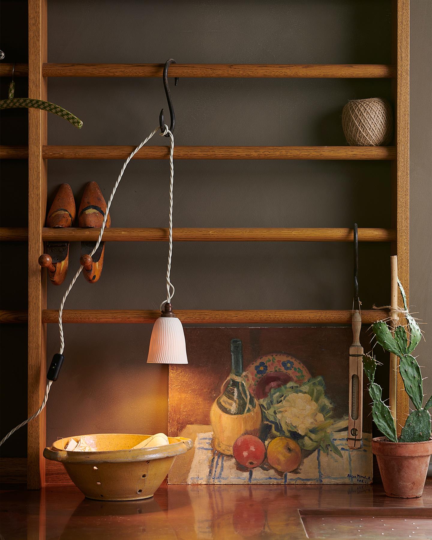 A Mediterranean-style kitchen with white painted cabinetry, white walls, terracotta flooring and an assortment of unglazed porcelain pendant lights hanging at various heights.
